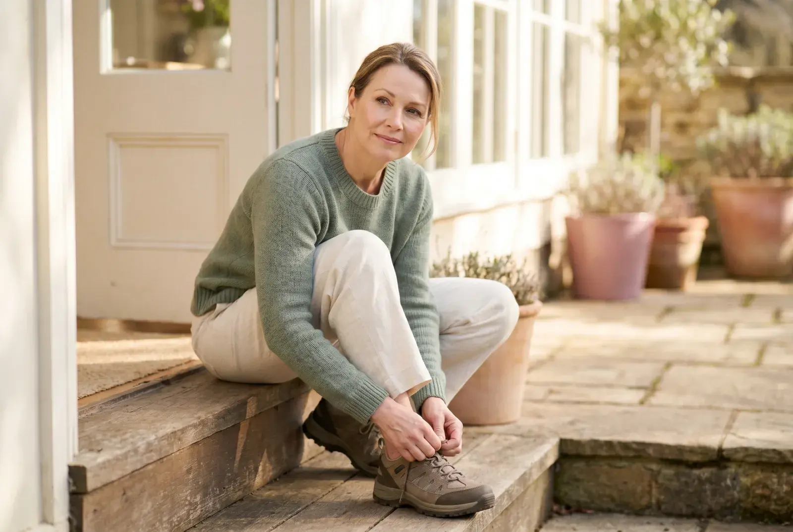 A woman lacing up walking shoes by an open, sunlit doorway